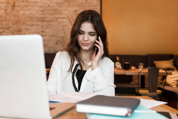 istock young beautiful woman working in her laptop having phone conversation with partner while drinking hot coffee in the cafe multitasking modern businesswoman 1203803271