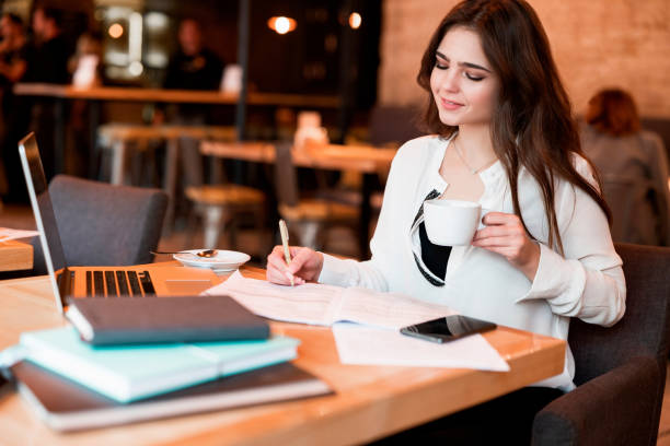 istock young beautiful woman working outside office in her laptop taking notes in her planner while drinking hot coffee in the cafe multitasking modern businesswoman 1203803273