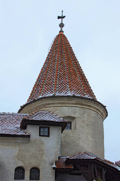 close up view of ancient tower with red tile roof in the snow, against cloudy sky. famous bran castle, also called dracula's castle. famous touristic place and travel destination in romania - vlad vi imagens e fotografias de stock