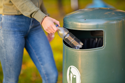 Midsection of young woman putting bottle in garbage bin. Female volunteer is cleaning park. She is dedicated towards environmental conservation.