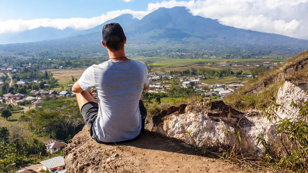 ruteng - un uomo seduto sulla collina con vista sull'isola vulcanica - flores man foto e immagini stock