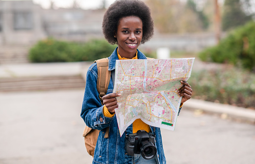 Beautiful smiling African-American woman holding a city map, checking out where to go next.