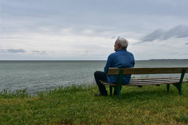 istock Senior man sitting on a bench and watching dark sea 1203810586