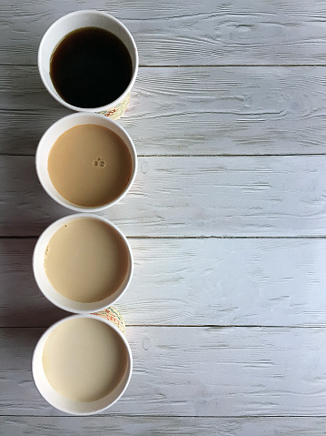 Four paper cups of coffee with milk on a wooden white background close up with space for copying. Flat lay