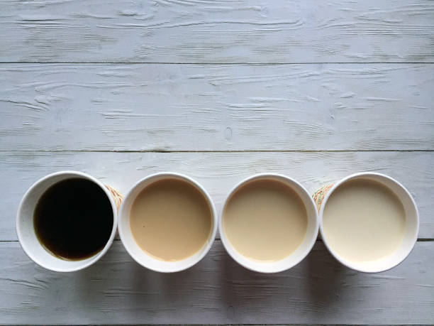 Four paper cups of coffee with milk on a wooden white background close up with space for copying. Flat lay