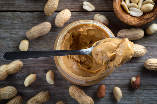Spoon and pot of peanut butter on wooden background - top view
