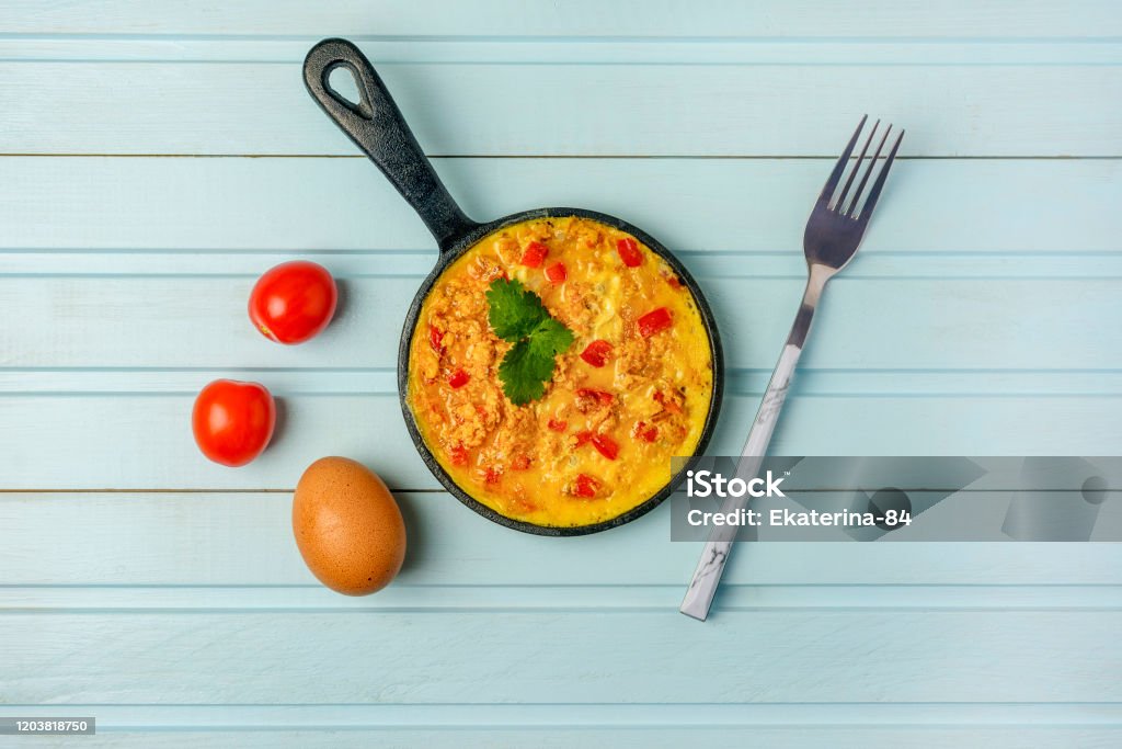 Freshly made omelet, Turkish national recipe Menemen with eggs, bell pepper and tomatoes. Photo on a blue background with copy space. Scrambled Eggs Stock Photo