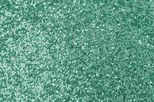 Bright shiny turquoise background for sites and layouts. The surface of many small sparkles, closeup. Selective focus.