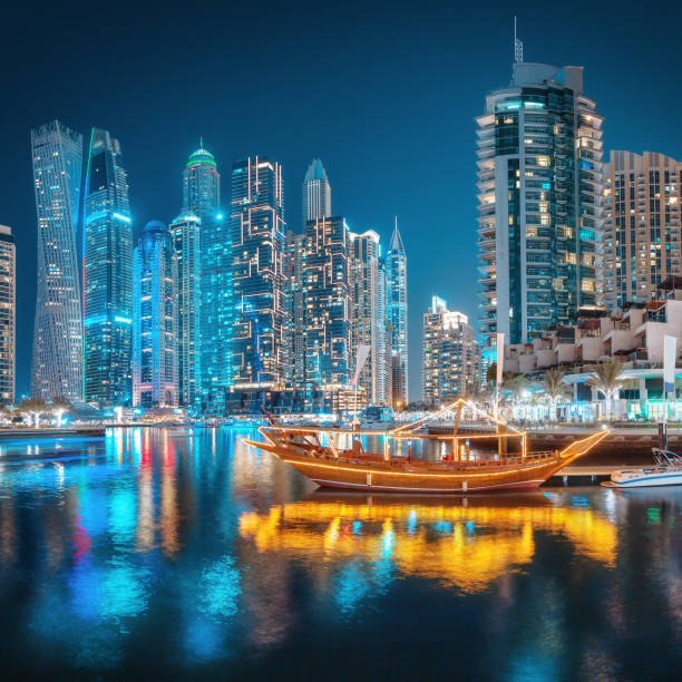 luci multicolori della città notturna nel quartiere dubai marina. stilizzata antica nave araba abra dhow con luci in primo piano. - dubai yacht luxury marina foto e immagini stock