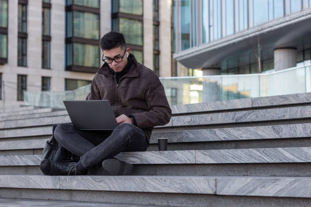 istock young male Asian student programmer freelancer work outdoors with laptop 1203821679