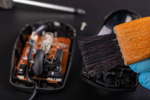 istock Cleaning of an optical computer mouse with a brush. Keeping the computer workplace clean. Dark background. 1203823146