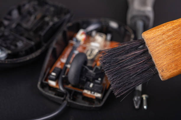 istock Cleaning of an optical computer mouse with a brush. Keeping the computer workplace clean. Dark background. 1203823213