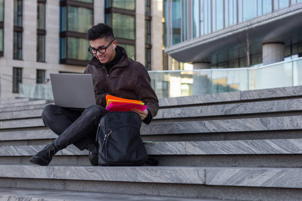 istock young happy Asian man student sit on the steps with laptop 1203823489