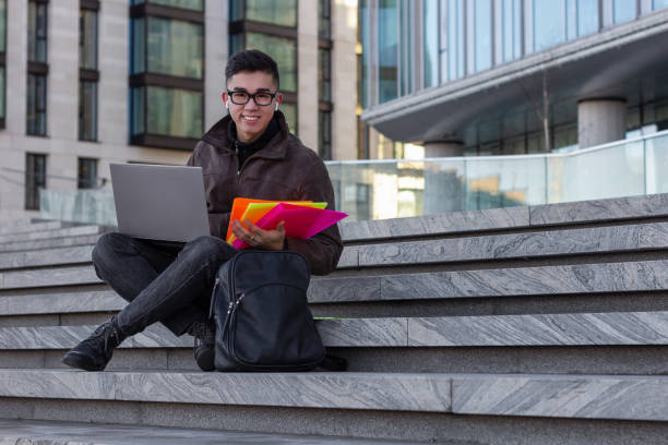 istock young happy Asian man student sit on the steps with laptop 1203823557