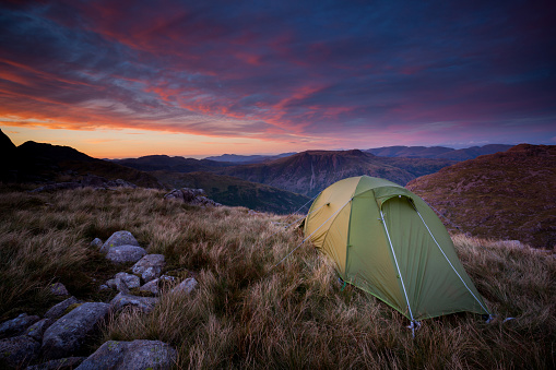 Green backpacking tent pitched for a wild camp on top of Cold Pike fell with a view of the Langdale Pike mountains in the English Lake District with a spectacular pink sunset.
