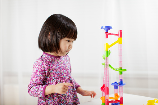 toddler girl play marble run game at home against white background