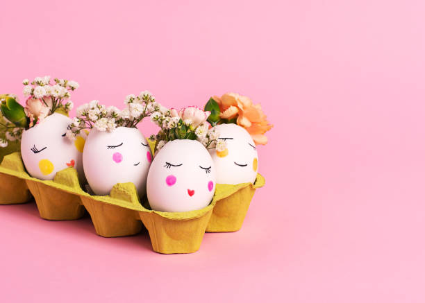 istock Easter creative concept. Easter decorative eggs with painted cheerful faces and flowers instead of hair in the cardboard egg tray on the pink backgraund. Copy space, close up 1203830104
