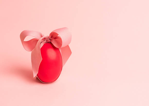 Easter creative concept. One red egg tied with a pink ribbon on a pink background. Minimalism, copy space, close up.