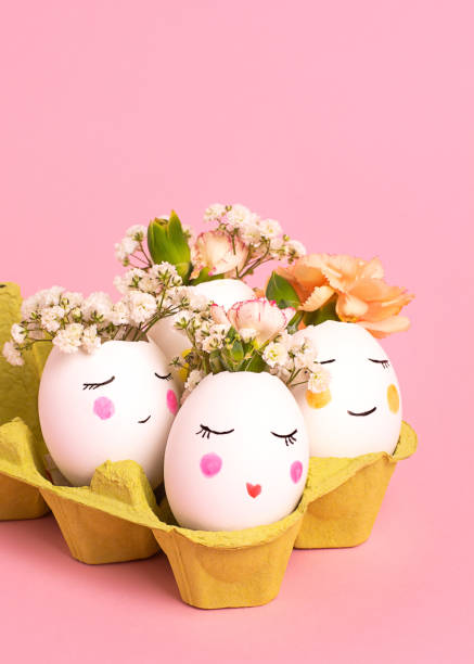 istock Easter creative concept. Easter decorative eggs with painted cheerful faces and flowers instead of hair in the cardboard egg tray on the pink backgraund. Copy space, close up 1203830161