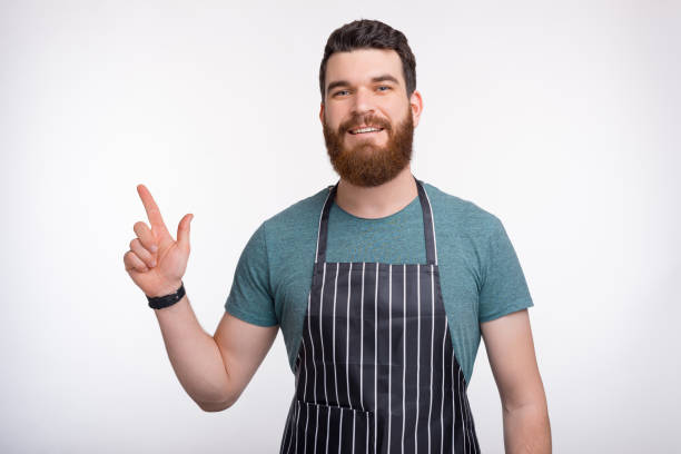 istock Photo of young bearded Chef pointing away at copyspace 1203831284