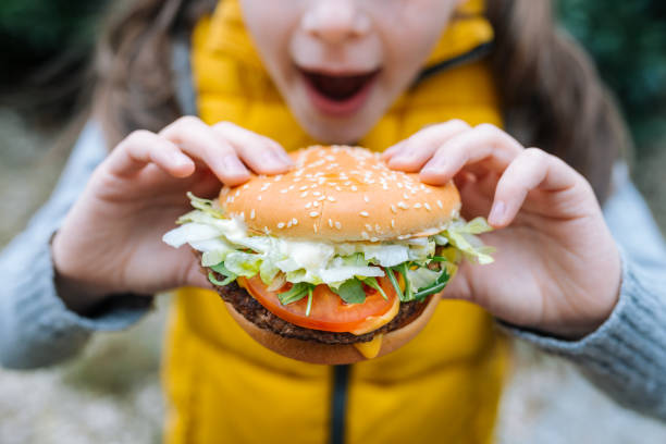 kleines mädchen isst einen großen cheeseburger mit tomaten, salat, rucola, rindfleisch und sauce - beautiful smiling vegetable calcium stock-fotos und bilder