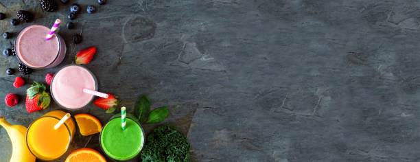 Banner with corner border of assorted healthy fruit smoothies against a dark stone background with copy space