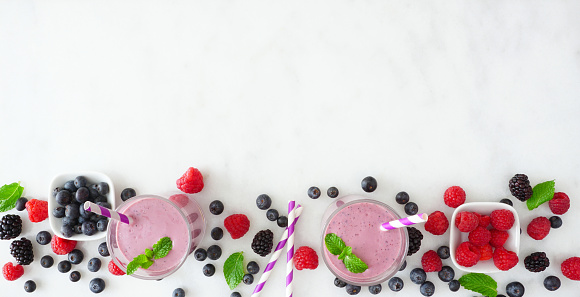 Banner with healthy mixed berry smoothie bottom border. Overhead view over a white marble background. Copy space.