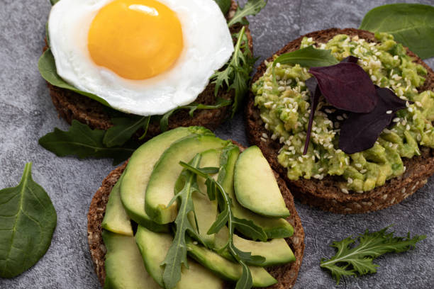 istock Avocado sandwich on dark rye bread with spinach and fried egg on a dark background 1203844014