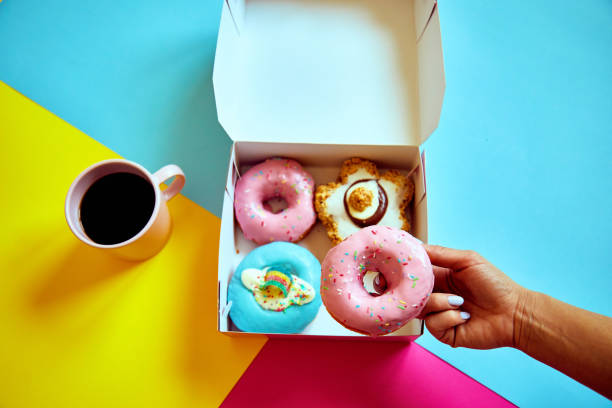 istock Sprinkled donuts in box and cup of coffee on colorful background. 1203845169