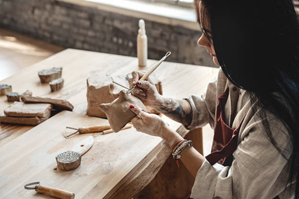 istock Craftsperson Concept. Young woman making pottery indoors making shape for clay using tool smiling happy close-up 1203854074
