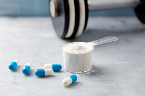 Scoop of Whey Protein, creatine capsules and a dumbbell. Bodybuilding food supplements on stone background. Close up.
