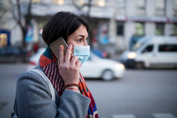 Young Woman With Face Mask Talking On The Phone. Side view of young woman with face mask walking on the street and talking on the phone. avian flu virus photos stock pictures, royalty-free photos & images