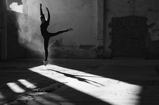 Silhouette of ballerina dancing in an abandoned building on a sunny day in black and white.