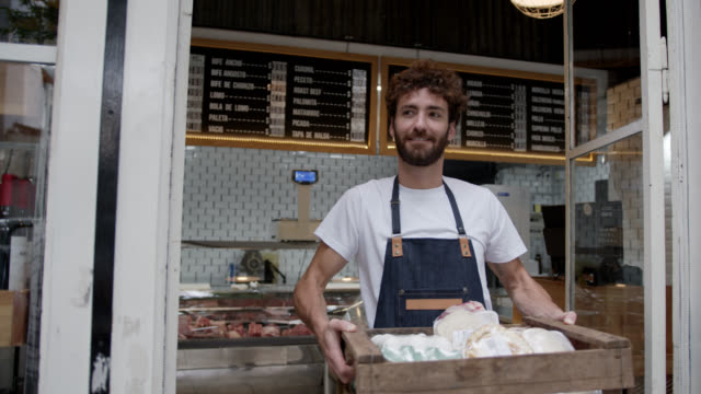 Cheerful employee of the deli leaving with a wood box with meat, eggs and other products for a delivery smiling