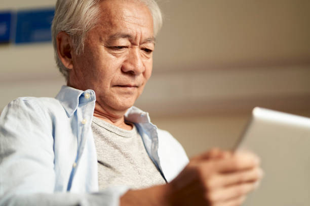 asiatischer alter mann mit blick auf digitales tablet - chinese culture china chinese ethnicity human face stock-fotos und bilder