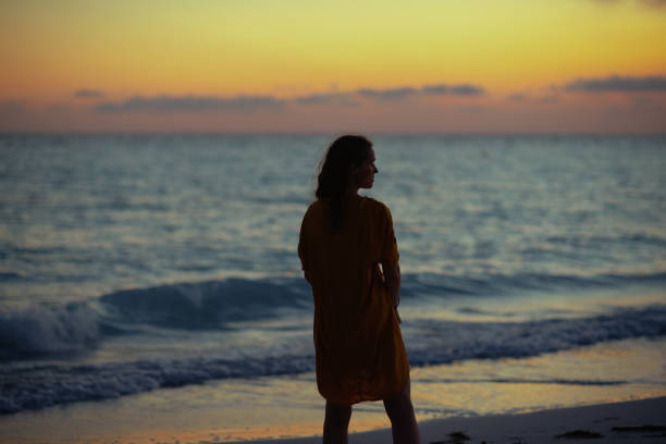istock trendy woman standing on seashore at sunset 1203891465