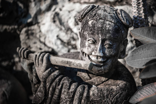 A stone statue of a Thai musician in the shady garden of a Buddhist temple in Central Bangkok.