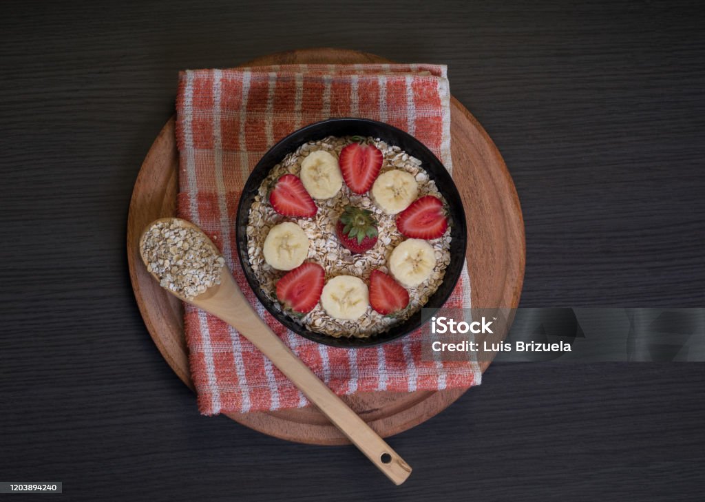 Aerial view of bowl with oatmeal and fruits Aerial view of a bowl with oatmeal and slices of bananas and strawberries with a wooden spoon with oatmeal, all on top of a round table and a rag Argentina Stock Photo