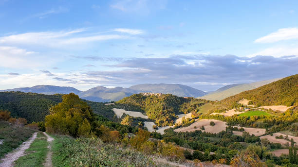 Panoramic Umbria landscape near Preci Poggio di Croce, Italy- October 16, 2019: A panoramic view of the mountain landscape of the Valnerina in rural Umbria, cultivated fields and farmland, autumn  is coming. single lane road footpath dirt road panoramic stock pictures, royalty-free photos & images