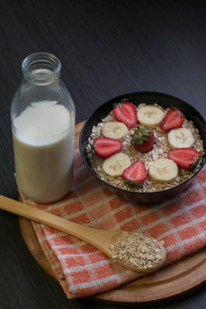 Bowl with oatmeal and fruits, milk bottle and wooden spoon with oatmeal stock photo