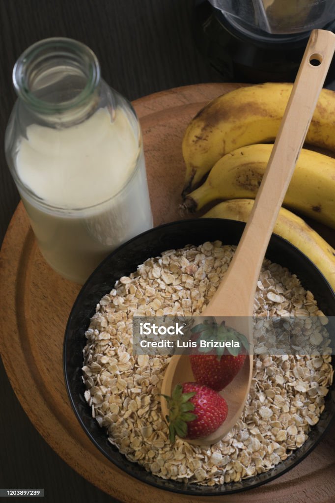 Strawberries oatmeal and bananas with a bottle of milk top plane of two strawberries in a wooden spoon on a bowl full of oatmeal with bananas and a bottle of milk around Argentina Stock Photo
