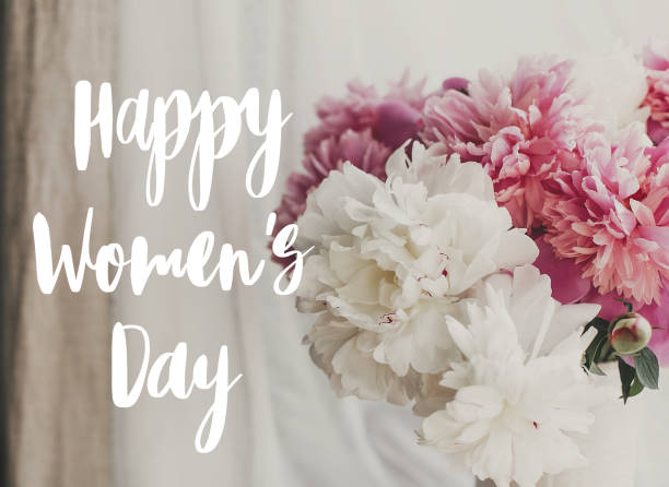 istock Happy Women's day text handwritten on lovely peony bouquet in sunny light on rustic  window sill. Stylish pink and white peonies in vase on wooden background. 8 march 1203903369
