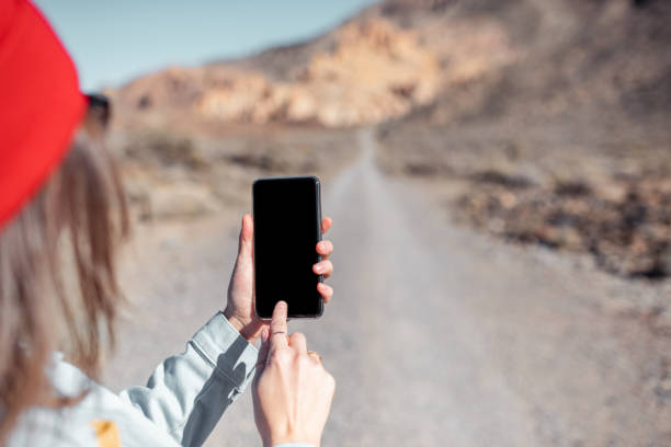 Mockup image of the smartphone with desert road on the background. Woman traveling with phone