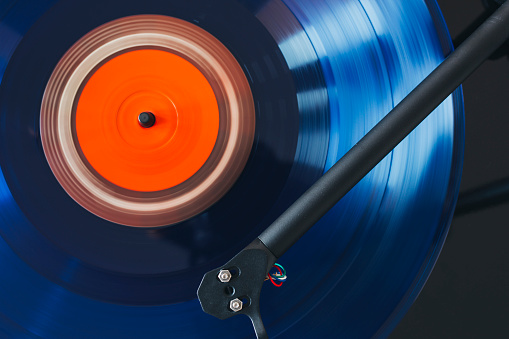 Close up of turntable tonearm playing blue vinyl record.