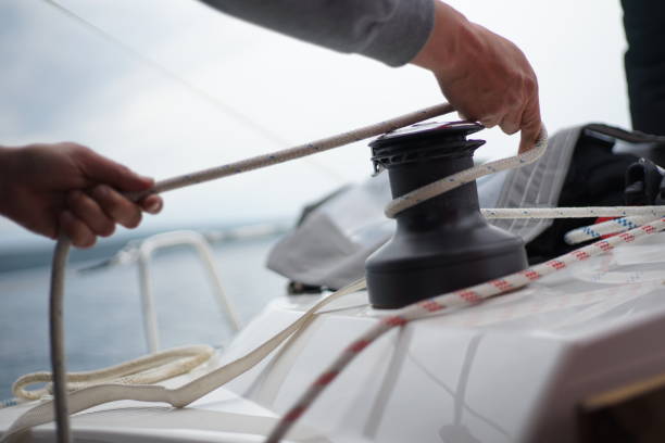 Hands of a man coiling up a rope, the halyard around the winch on a sailboat stock photo