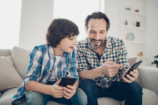 Sms message modern technology digital world generation concept. Photo of mature, bearded excited guy showing new social page site shop with electronic toys to his younger son sitting on divan
