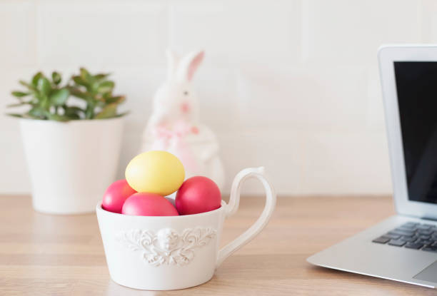 Easter Eggs in White Bowl, Laptop, Rabbit, Succulent On The Kitchen Counter, Close Up. Kitchenware In Modern Kitchen Interior. White Tiles Background