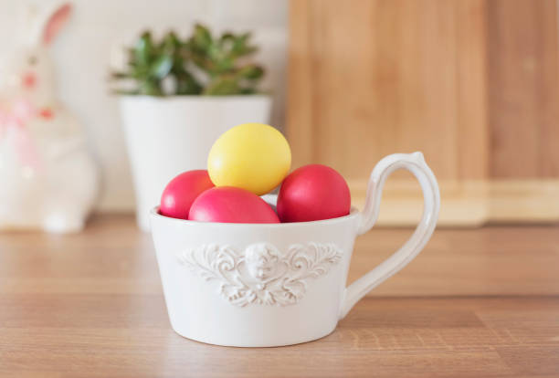 Happy Easter! Colorful Easter Eggs in White Bowl, Rabbit, Succulent On The Kitchen Counter, Close Up. Kitchenware In Modern Kitchen Interior. White Tiles Background