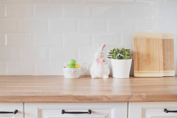 Happy Easter! Easter Eggs, Rabbit, Cutting Boards, Succulent On The Kitchen Counter. Bright And Clean Rustic Kitchen With White Cabinets, Close Up. Kitchenware In Modern Kitchen Interior. White Tiles Background