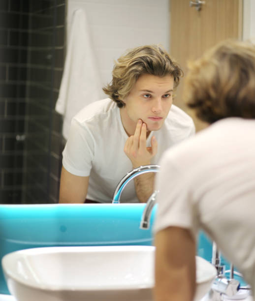 istock young man looking in the mirror,combing his hair,looking at problems on face 1203932598